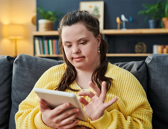 Young woman with Down syndrome using a tablet device at home for online NDIS TeleHealth continence assessment.