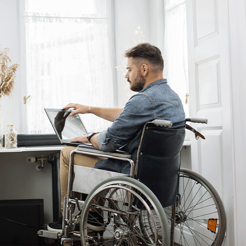 Man in a wheelchair working on a laptop at home, representing continence assessment and NDIS support services in Alice Springs, Northern Territory.