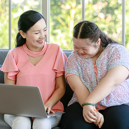 Carer supporting a young woman while using a laptop, symbolising personalised continence care and disability support in Tasmania.