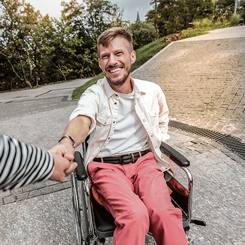 Smiling man in a wheelchair being supported outdoors, representing independence and continence support services in Canberra, ACT.