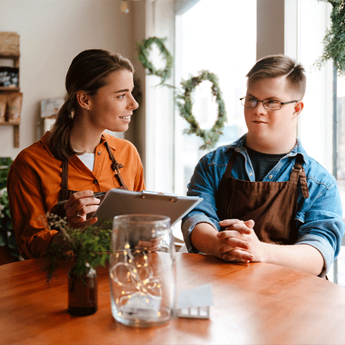 Support worker talking with a young man with disability at a table, representing personalised continence assessment and NDIS support services in Ridgehaven, SA 5097.