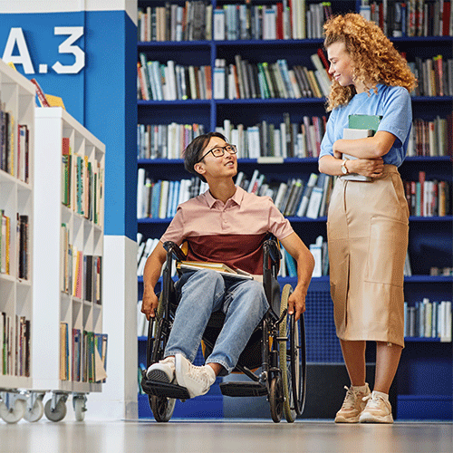 Young person in a wheelchair talking with a support worker in a library, representing disability and continence support services in Toongabbie, NSW.