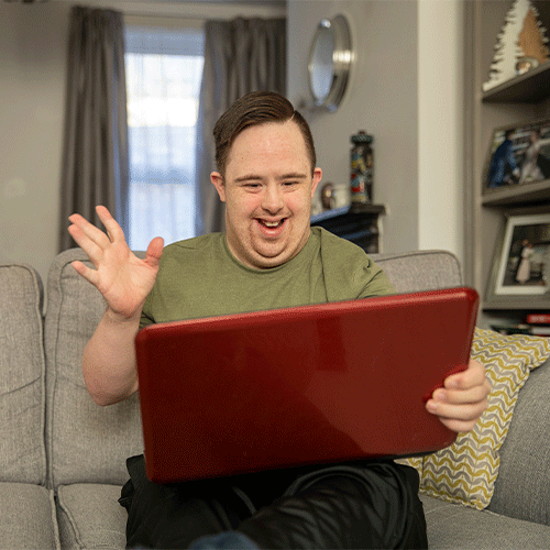 Young man with disability smiling and using a laptop at home, representing inclusive disability and continence support services in Willetton WA 6155.<br>