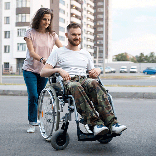 Support worker assisting a man in a wheelchair toward a vehicle, symbolising community access and continence-related support services in Woree, Queensland.