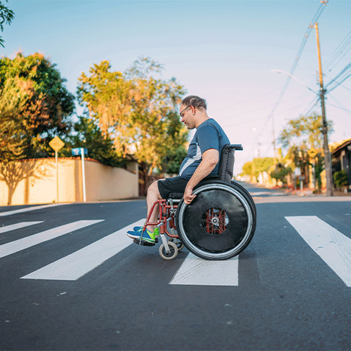 Person using a wheelchair crossing the street in an urban area, representing accessible disability and continence support services in Footscray, Victoria.