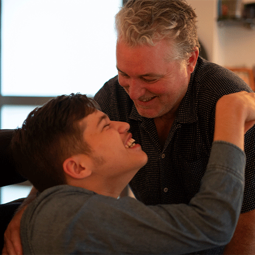A young NDIS participant laughing with his carer at home in Australia