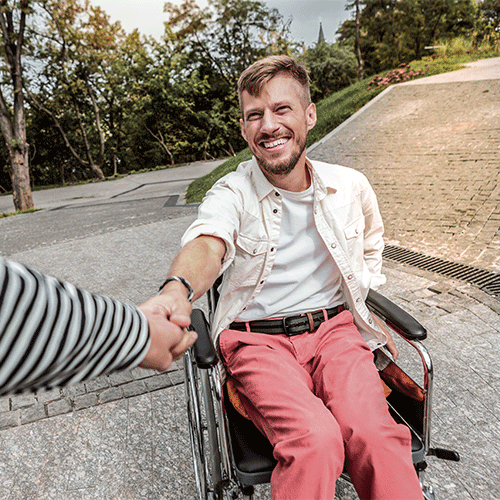 Smiling NDIS participant in a wheelchair holding hands with a carer outdoors — continence assessment services in Bayswater, Vic