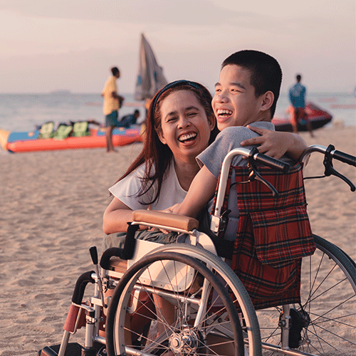Happy young NDIS participant in a wheelchair laughing with a carer on the beach — A1 Care Group continence assessment services