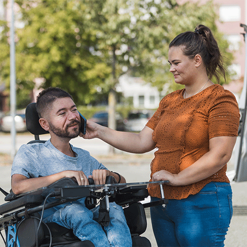 NDIS support worker assisting a man in a power wheelchair outdoors in Wollongong NSW