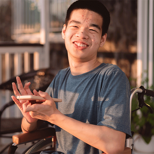 Young man with disability smiling and using a smartphone while seated in a wheelchair outdoors
