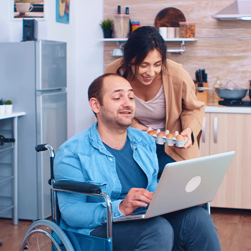 NDIS participant in a wheelchair using a laptop to book a continence assessment in Nunawading, Vic while his carer offers support at home